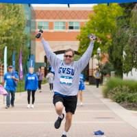 Participant crossing finish line celebrating with two hands in the air